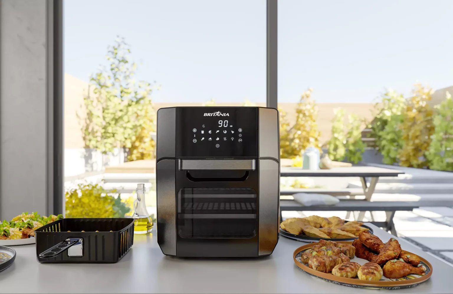 Air fryer oven Britânia posicionada ao centro de uma bancada ao ar livre, com visor digital aceso em 90 graus. Ao redor do eletrodoméstico, pratos com diversos alimentos assados como frango, pãezinhos e salgados, além de uma assadeira com legumes e uma garrafa de azeite. Ao fundo, área externa com mesas e vegetação, sugerindo uma refeição prática e saborosa em um dia ensolarado.