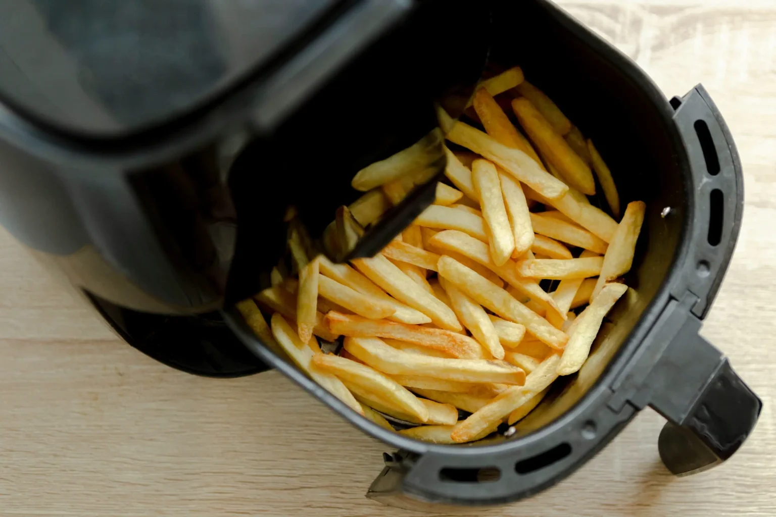 Cesta de air fryer aberta com batatas fritas congeladas assadas, já douradas e crocantes. A imagem mostra o preparo prático e sem óleo, destacando a eficiência do eletrodoméstico para quem busca refeições rápidas e mais saudáveis.