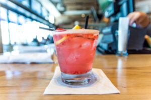 Coquetel rosa com gelo, frutas cítricas e frutas vermelhas servido em copo baixo sobre guardanapo em um bar iluminado