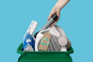 Eletrodomésticos e eletrônicos usados sendo colocados em uma lixeira verde de reciclagem, representando o descarte sustentável de aparelhos domésticos.