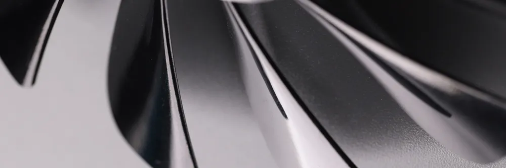 Hélice de ventilador em close-up, mostrando pás de metal com acabamento escuro e formato curvo, destacando resistência e design para ventilação mais intensa.