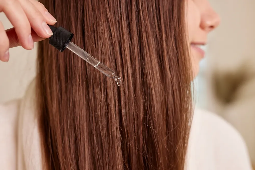Uma jovem aplica uma gota de óleo com uma pipeta nos cabelos, em close-up. Vitaminas e queratina para tratamento, fortalecimento e crescimento capilar. Problemas com caspa e queda de cabelo. Conceito de cuidados com os cabelos.