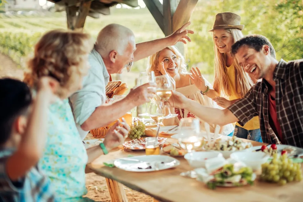 Família multigeracional desfrutando de um almoço em família no pátio de um vinhedo.