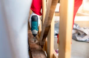 Técnico perfurando uma caixa de madeira com uma furadeira. Montagem de caixas para transporte de maquinário pesado. Técnicos carpinteiros usam luvas de segurança ao manusear furadeiras elétricas para perfurar tábuas.