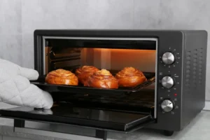 Mulher retirando do forno elétrico uma assadeira com pãezinhos em espiral deliciosos, em close
