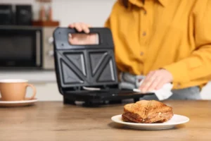 Sanduíche tostado recém-feito no prato com a pessoa que limpa sanduíche na cozinha, no fundo, uma pessoa com uma camisa amarela limpa uma sanduíche com um pano branco