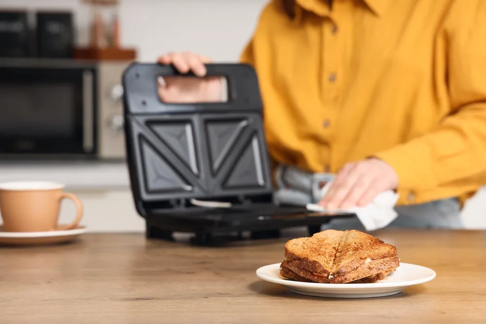 Sanduíche tostado recém-feito no prato com a pessoa que limpa sanduíche na cozinha, no fundo, uma pessoa com uma camisa amarela limpa uma sanduíche com um pano branco